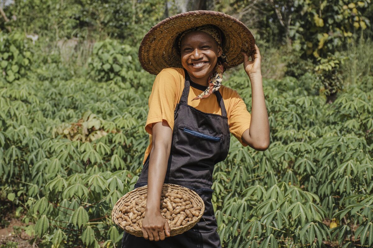 A smiling African woman farmer holding a basket of harvest in her field