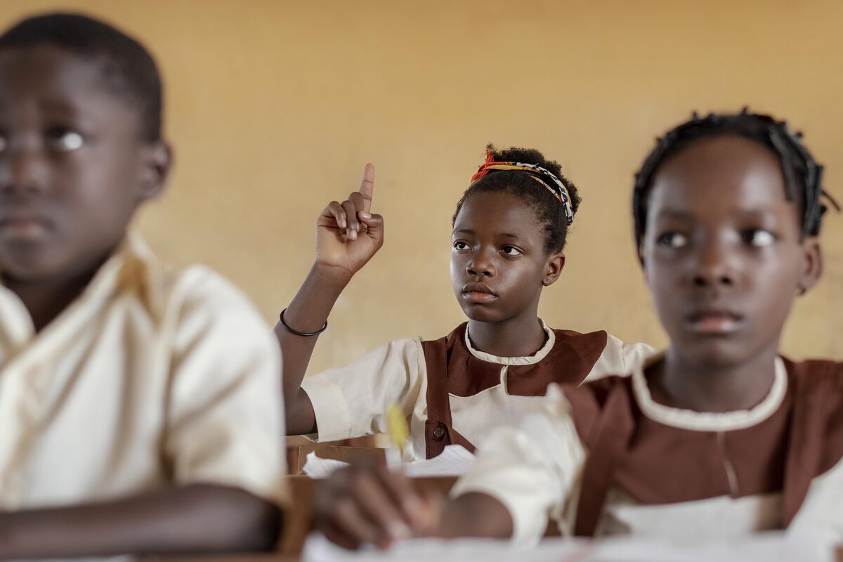 African schoolchildren in a classroom, one raising her hand to answer